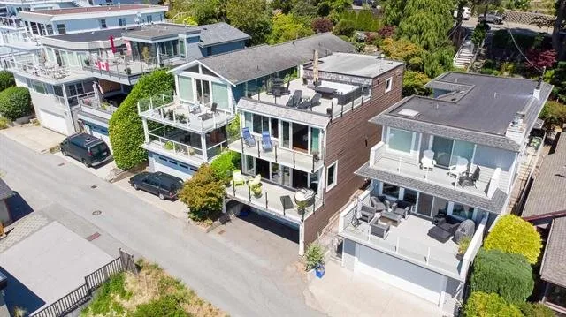 Aerial view of the finished multi-level home showing rooftop deck, glass railings, and outdoor lounge furniture.