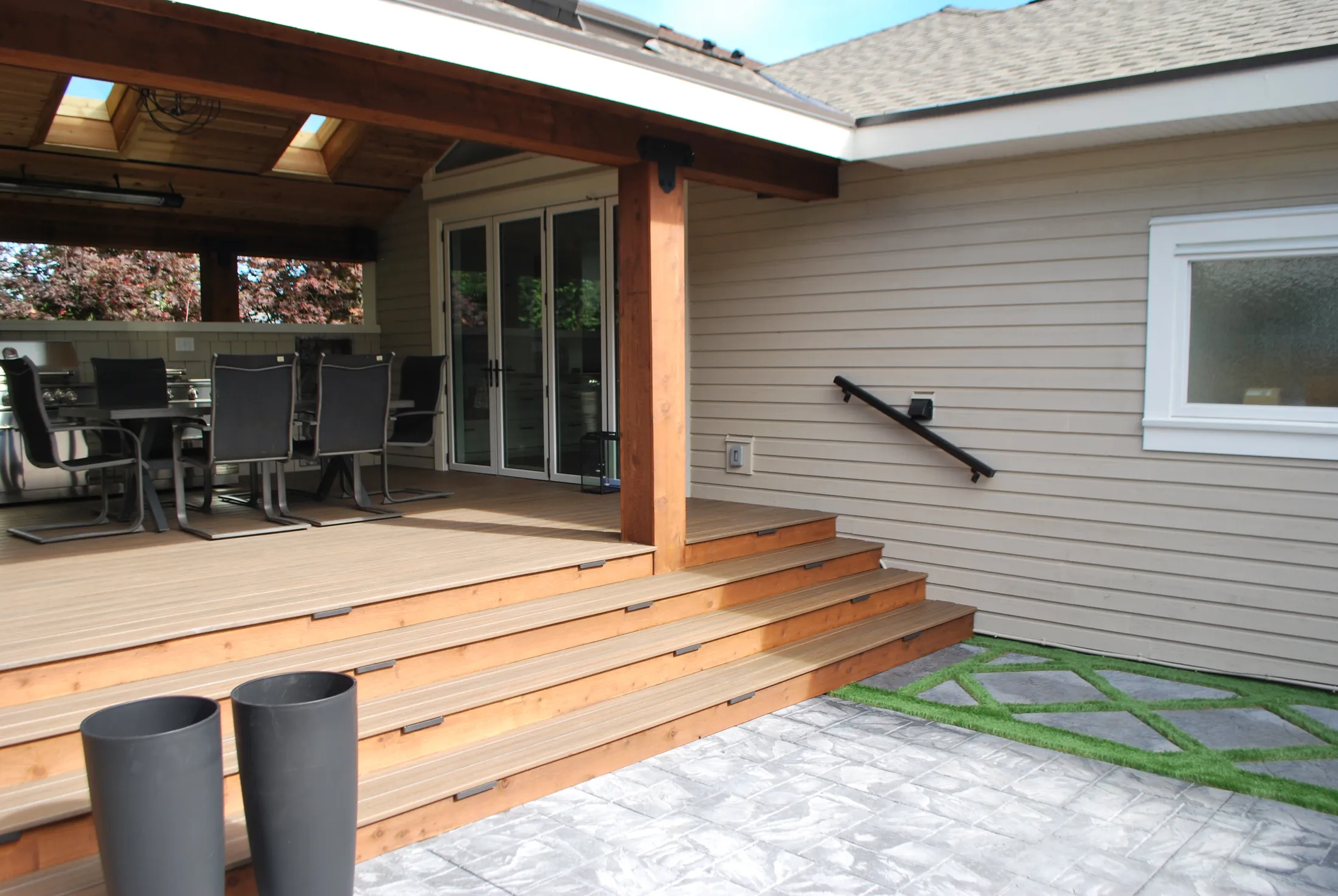 Wood deck steps leading down to the stamped-concrete patio, with the covered outdoor kitchen visible above.